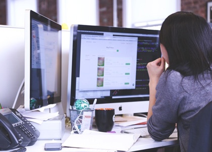 Image of woman sitting at computer looking over data analytics.