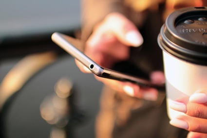 Image of woman holding coffee and smartphone. Phone calls can help increase conversion rates.