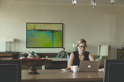 Image of woman sitting at table on laptop. Customers matter in website design.